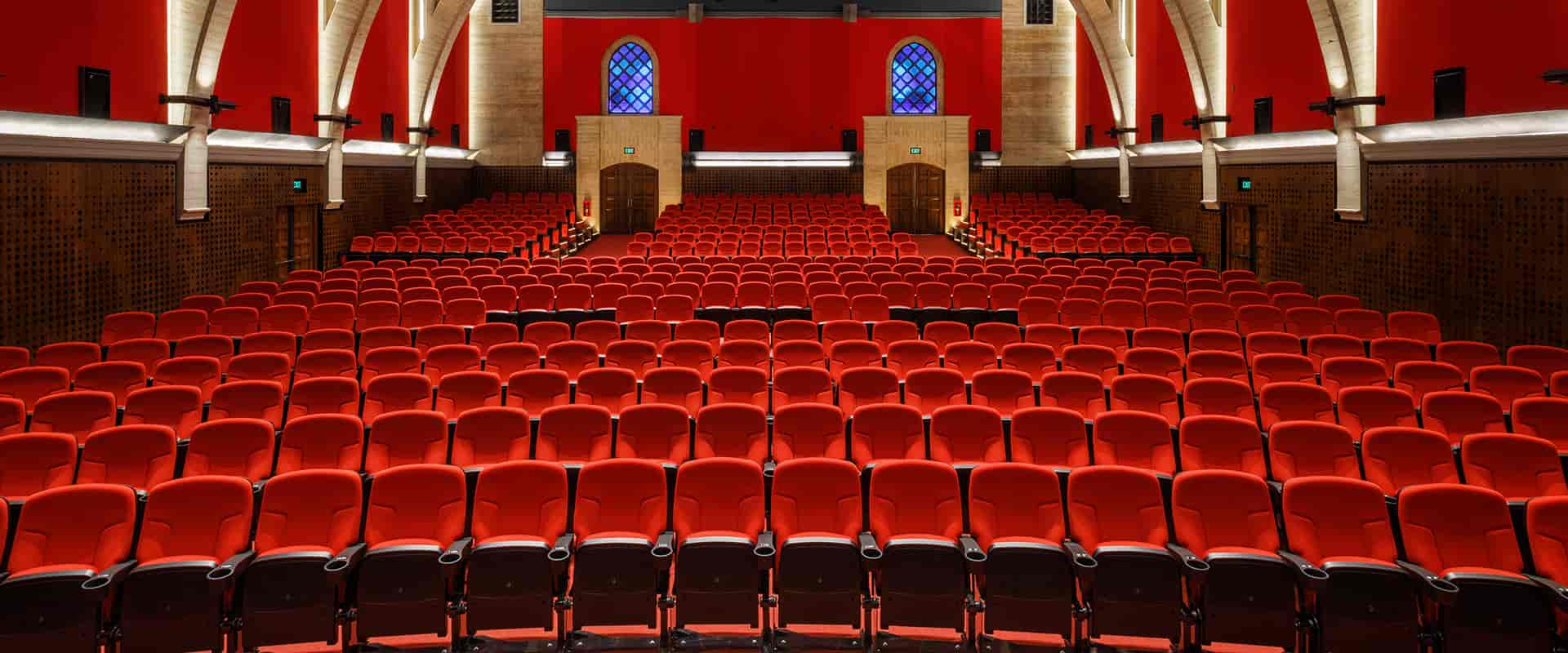 Grande salle remplie de rangées de sièges rouges, vue depuis le fond vers la scène