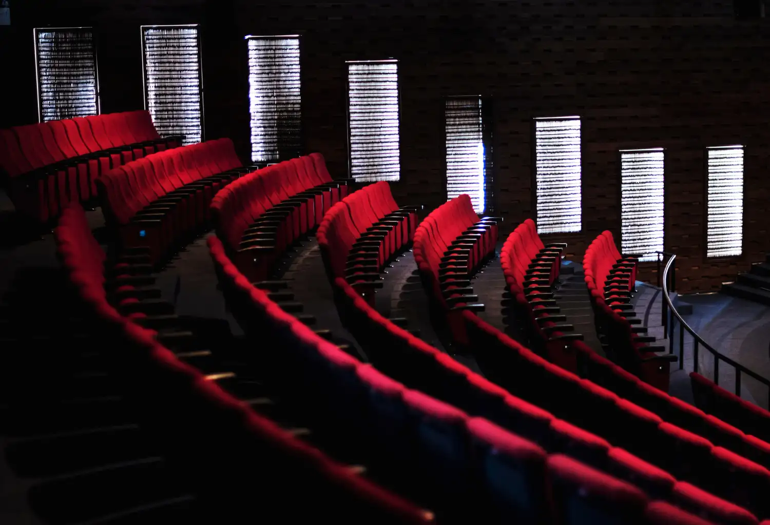 Aménagement des sièges d’auditorium avec des rangées courbes de fauteuils rouges face à un mur lumineux