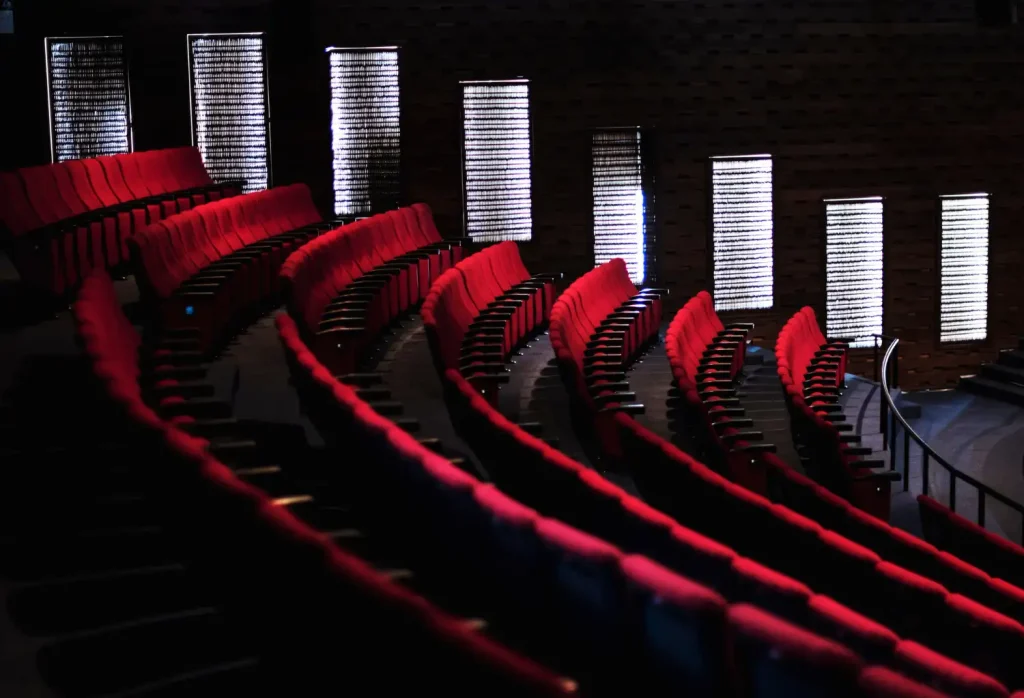 Auditorium seating layout with curved rows of red tip-up seats facing a backlit wall