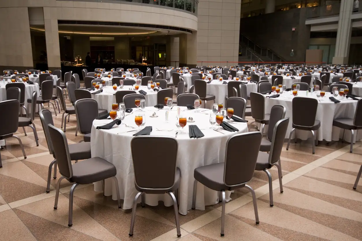 Round banquet tables set with white linen and dark brown stackable banquet chairs in a hotel hall